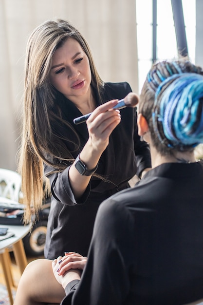 Maquillage de femme maître appliquant le teint de la peau poudre de fond de teint blush sur le visage utiliser le pinceau au salon de beauté