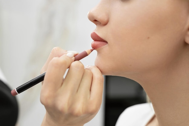 Maquillage des lèvres. Plan rapproché d'un cosmetologist peignant ses lèvres avec un crayon avant le maquillage permanent