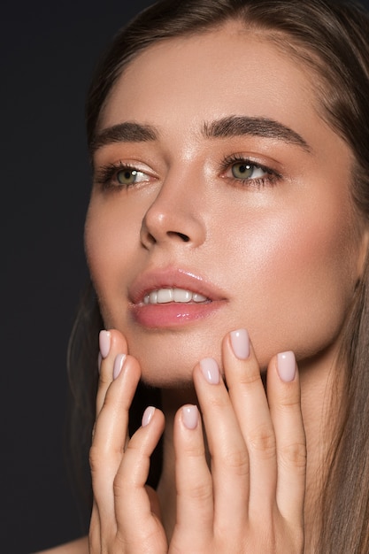 Maquillage naturel beauté femme, peau saine, cheveux lisses. Fond sombre. Prise de vue en studio.