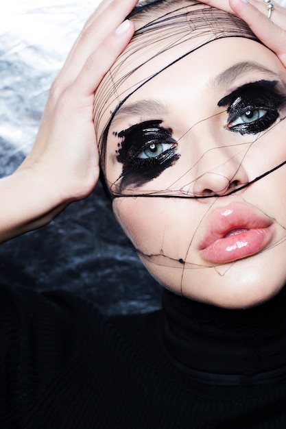 Maquillage noir humide devant les yeux. Portrait de beauté créative d'une fille avec des strass et du rouge à lèvres barbouillé.