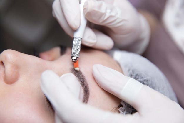 Maquillage permanent pour les sourcils. Microblading des sourcils. Esthéticienne faisant le tatouage des sourcils pour le visage féminin. Belle jeune fille dans un salon de beauté