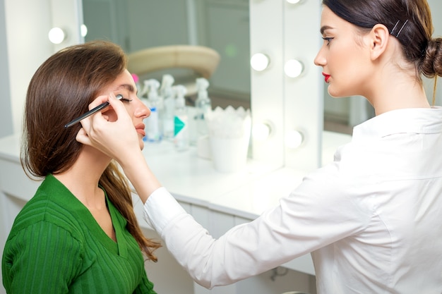 Maquilleur applique la poudre de fard à paupières sur les yeux de la jeune femme de race blanche par l'outil de brosse dans un salon de beauté