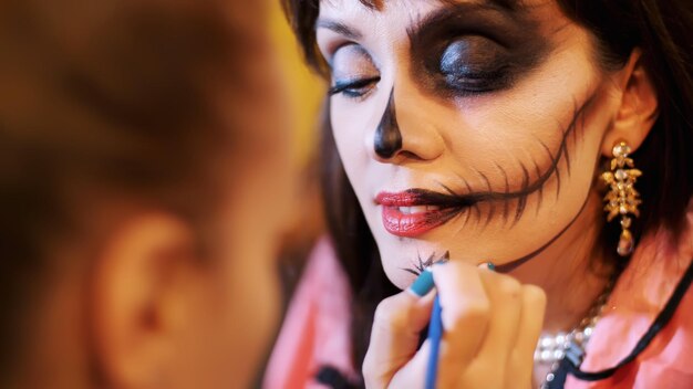 Le maquilleur de la fête d'Halloween dessine un terrible maquillage sur le visage d'une femme brune.