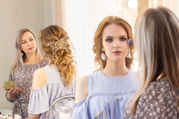 Maquilleur met le maquillage sur le modèle de la fille. Le pinceau applique les ombres, le correcteur. modèle de belle fille, portrait. Couleurs nues dans le maquillage. maquillage de mariage, maquillage de soirée.