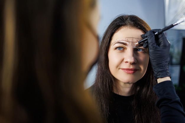 Photo un maquilleur permanent marque les sourcils d'une femme avec un crayon procédure cométologique de maquillage permanent soins pour le visage d'une femme