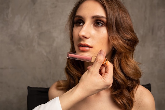 Un maquilleur professionnel choisit un rouge à lèvres pour un modèle de fille sur fond gris avec une place pour le texte