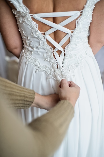 Une maquilleuse aide la mariée à nouer sa robe de mariée