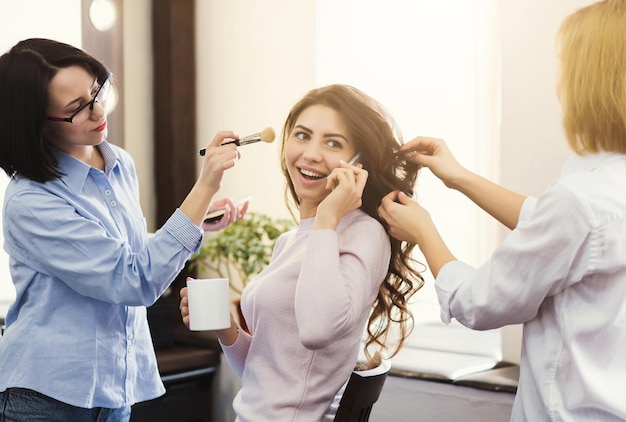 Maquilleuse et coiffeuse travaillent en tandem, modèle curl et couleur qui parle au téléphone dans un salon de beauté