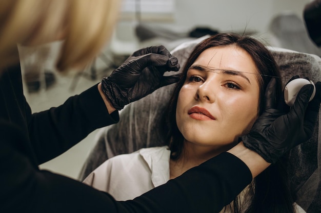 Photo la maquilleuse épile les sourcils avec un gros plan de fil cosmétologie féminine dans le salon de beauté