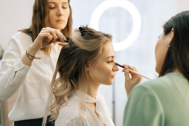 Maquilleuse de mariage faisant du maquillage de mode pour une belle mariée dans un dressing d'éclairage