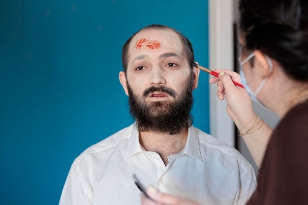 Maquilleuse utilisant des effets spéciaux pour créer un costume de zombie et un look effrayant de cadavre dramatique. Homme ayant l'air décédé et infecté après avoir eu des cicatrices sanglantes et un visage de monstre, un design effrayant.