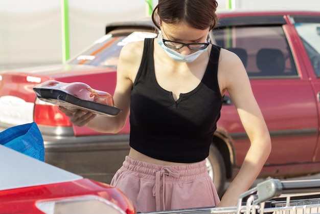 Marchandises de supermarché épicerie et nourriture une jeune femme met les produits d'un chariot dans le coffre d'une voiture