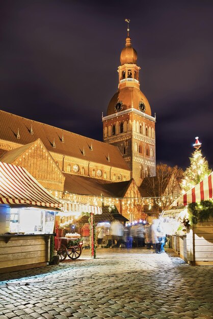 Marché de Noël sur la place du Dôme près de la cathédrale de Riga dans le vieux Riga, Lettonie. C'est la plus ancienne église médiévale des États baltes. Flou de mouvement. Mise au point sélective