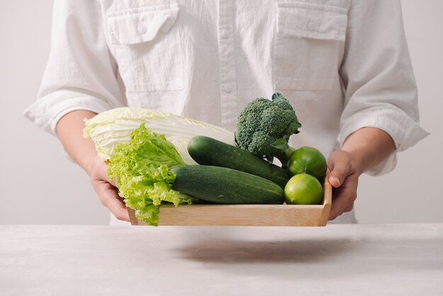 Marché. Nourriture végétalienne saine. Légumes frais, baies, légumes verts et fruits dans un plateau en bois : concombres radis pois verts... tableau blanc. Dans les mains de l'homme, copiez l'espace