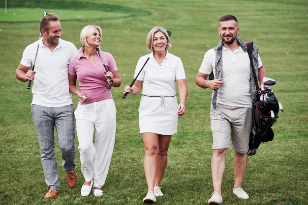 Marcher sur la pelouse. Des amis joyeux passent du temps sur le terrain de golf avec des bâtons et de la bonne humeur.