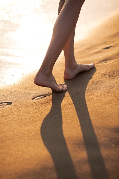 Photo marcher pieds nus le long du surf sur la plage de sable au coucher du soleil