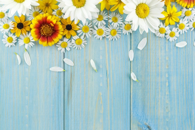 Marguerites blanches et fleurs de jardin sur une table en bois usée bleu clair.