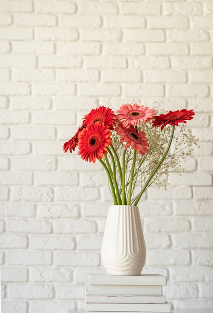 Marguerites gerbera rouges et roses dans un vase blanc sur une pile de livres, style minimal, conception de maquette