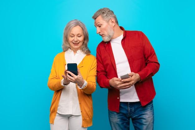 Photo un mari âgé jaloux regardant le smartphone de sa femme sur un fond bleu.