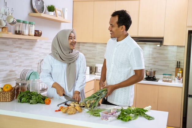 Le mari aide sa femme dans la cuisine. couple asiatique musulman préparant le dîner ensemble. un jeune homme et une femme romantiques s'amusent à préparer de la nourriture à la maison