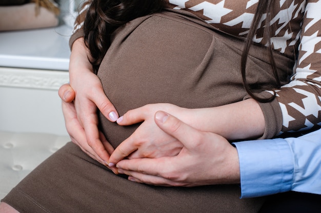 Un mari attentif serre tendrement sa femme enceinte et ses mains reposent sur son ventre en forme de cœur