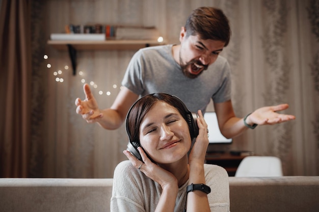 Mari en colère criant à sa femme assise sur un canapé et couvrant les oreilles avec des écouteurs