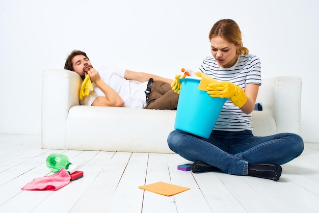 Le mari est allongé sur le canapé pendant que sa femme nettoie les travaux intérieurs