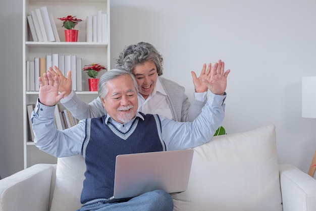 Le mari et la femme âgés assis sur un canapé regardent un ordinateur portable sont heureux