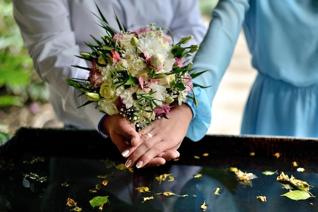 mari et femme mains près de l'eau et des fleurs bouquet de mariage