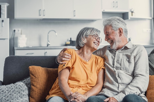 Photo un mari et une femme mûrs heureux s'assoient et se reposent sur le canapé à la maison en s'étreignant et en se caressant, en montrant de l'affection, en souriant, en étant âgés, en s'aimant, en se relaxant sur le canappé, en samusant, en profitant d'un week-end familial tendre et romantique.