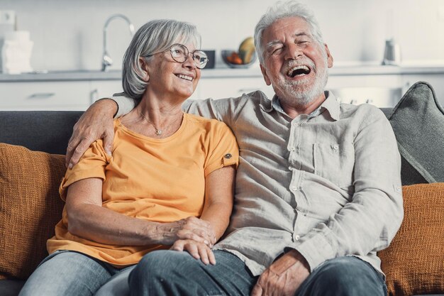 Photo un mari et une femme mûrs heureux s'assoient et se reposent sur le canapé à la maison en s'étreignant et en se caressant, en montrant de l'affection, en souriant, en étant âgés, en s'aimant, en se relaxant sur le canappé, en samusant, en profitant d'un week-end familial tendre et romantique.