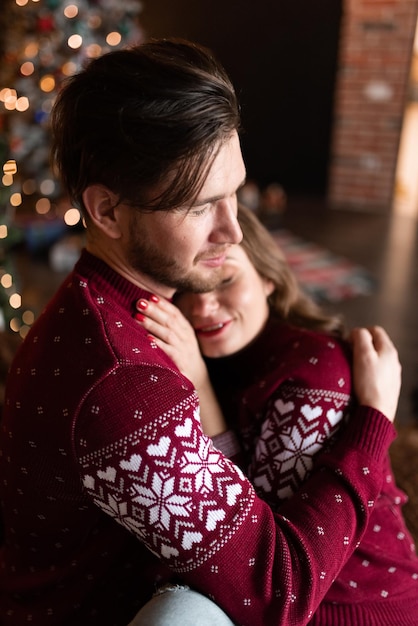 Mari et femme portant des chandails tricotés identiques s'amusent ensemble à célébrer Noël Couple ensemble sur le lit Les amoureux sont dans une chambre de style loft joliment décorée