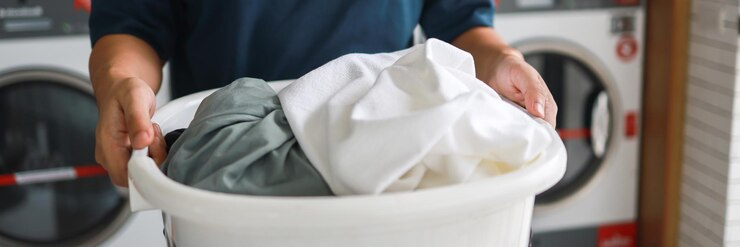 Mari de maison avec panier et linge sale lavé les vêtements dans la machine à laver intérieure de la buanderie au magasin de blanchisserie