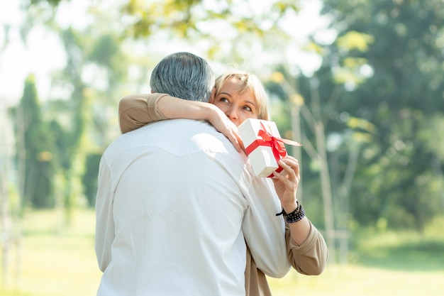 Le mari prend un cadeau à sa femme surprise dans le parc vieux couple d'amour dans le concept de la Saint-Valentin