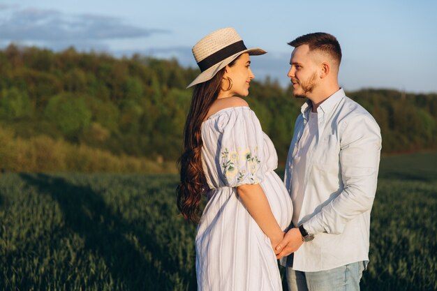 Le mari et sa femme enceinte se promènent au coucher du soleil dans un champ à l'extérieur. Thème de la grossesse romantique à l'extérieur.