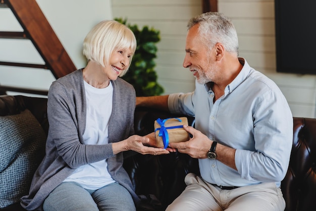 Mari senior souriant faisant la surprise et donnant une boîte-cadeau à sa femme