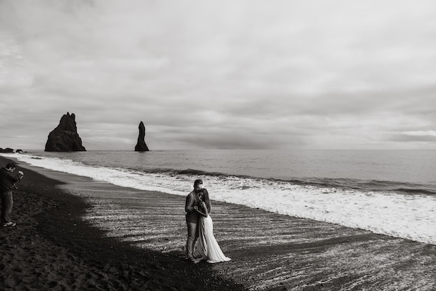 Mariage à destination de l'Islande. Un couple de mariés se promène le long de la plage noire de Vic.