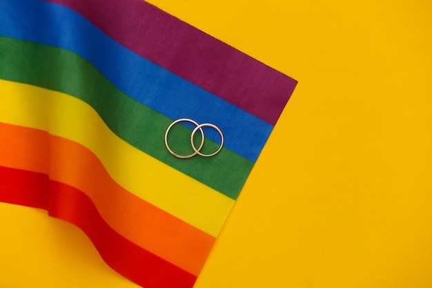 Mariage LGBT. Drapeau arc-en-ciel LGBT et anneaux dorés sur fond jaune. Tolérance, liberté