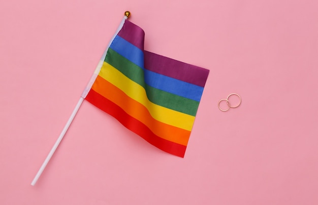 Photo mariage lgbt. drapeau arc-en-ciel lgbt et anneaux dorés sur fond rose. tolérance, liberté