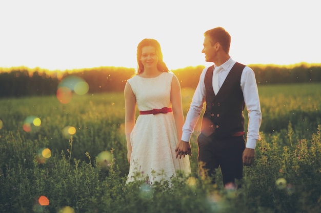 Mariage. La mariée et le marié se tiennent la main et marchent dans le parc à la lumière du coucher du soleil