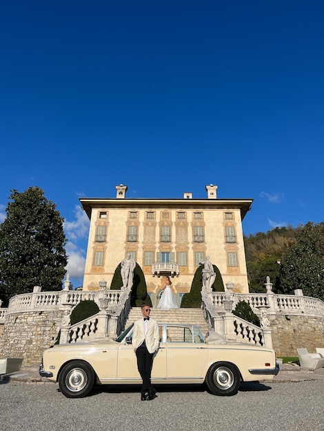 Le marié attend près de la voiture que la mariée descende les marches d'une ancienne villa