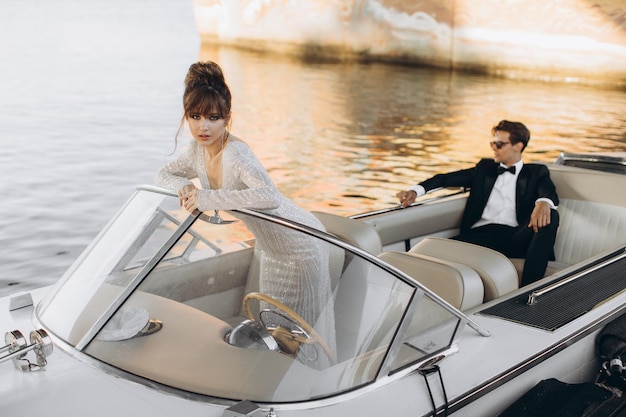 Le marié en costume noir et lunettes de soleil embrasse la mariée en robe de mariée sur un yacht par une journée ensoleillée