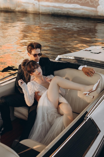 Le marié en costume noir et lunettes de soleil embrasse la mariée en robe de mariée sur un yacht par une journée ensoleillée