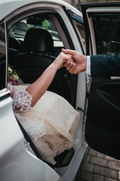 Le marié donne les mains à la mariée de la voiture de mariage