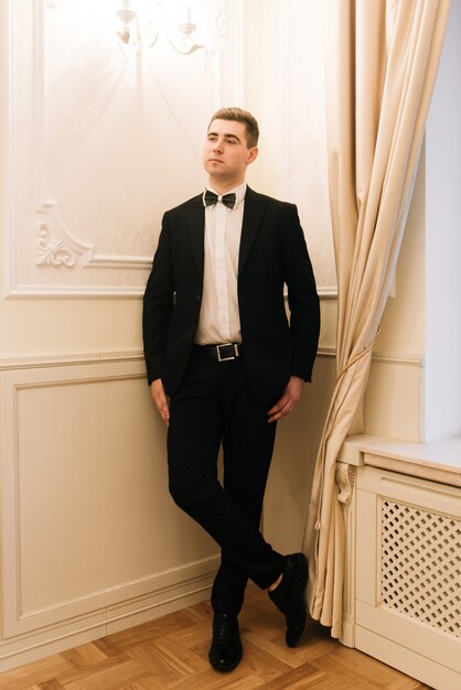 Marié élégant mettant le costume et le noeud papillon. Portrait d'homme confiant et heureux. Le marié se prépare le matin. Photo de mariage créative