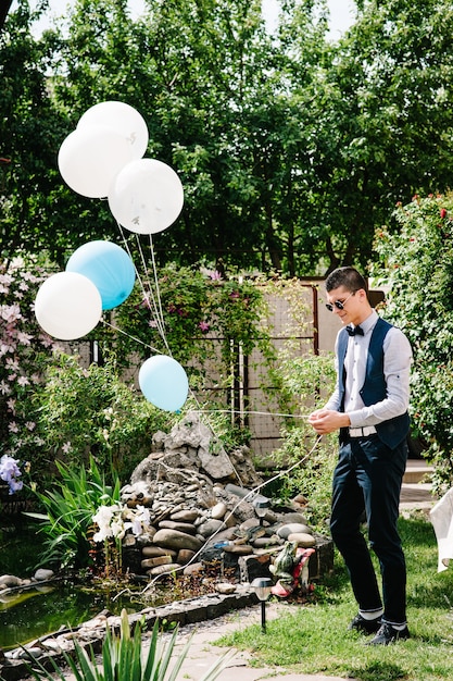 Le marié élégant porte des ballons à la fontaine dans la cour.