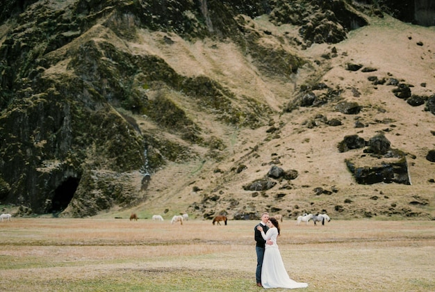 Le marié embrasse la mariée sur fond de chevaux broutant au pied de la montagne Islande