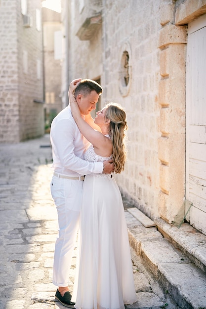 Photo le marié embrasse la mariée par la taille près de la vieille maison de pierre