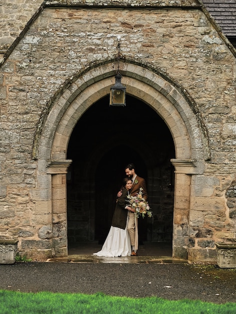 Photo le marié embrasse la mariée près de la vieille église anglaise, temps nuageux.