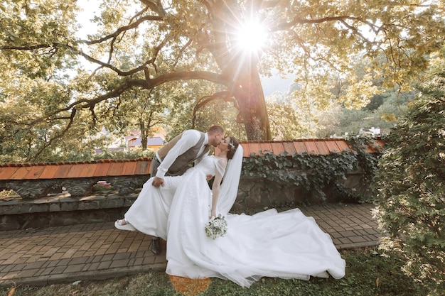 Photo le marié embrasse passionnément la mariée, s'appuyant sur elle comme dans une danse sur le fond de la nature par une chaude journée d'été.